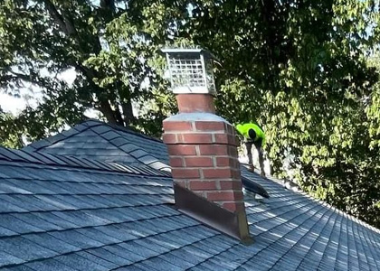 Repaired metal flashing around a brick chimney on an asphalt shingle roof